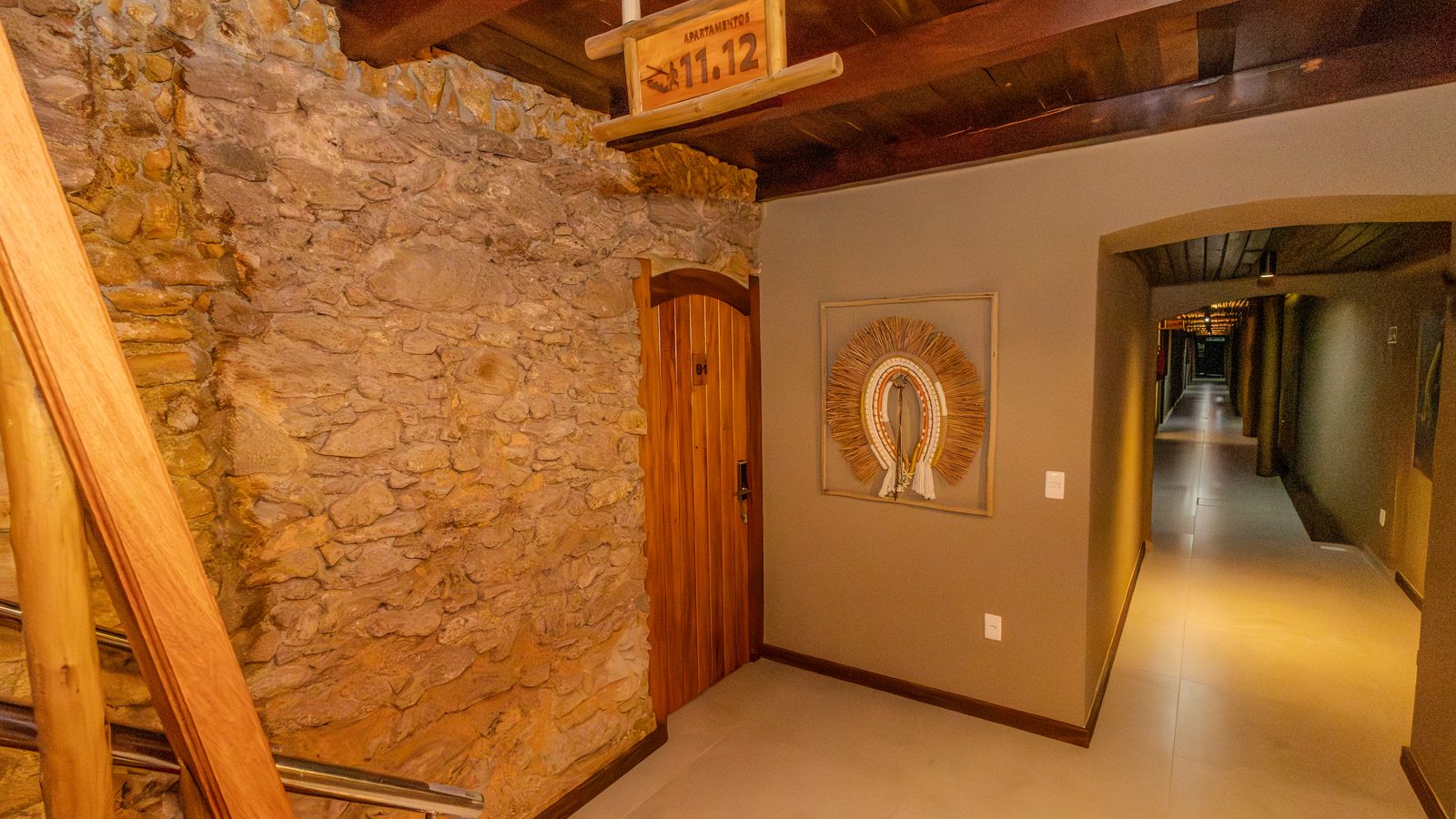 Hall de acesso aos apartamentos, com teto de madeira e parede de pedra
