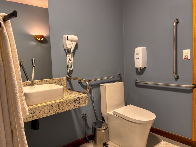 Banheiro do Apartamento PCD, com barras de apoio ao lado do vaso e da pia, e pia sem armário embaixo